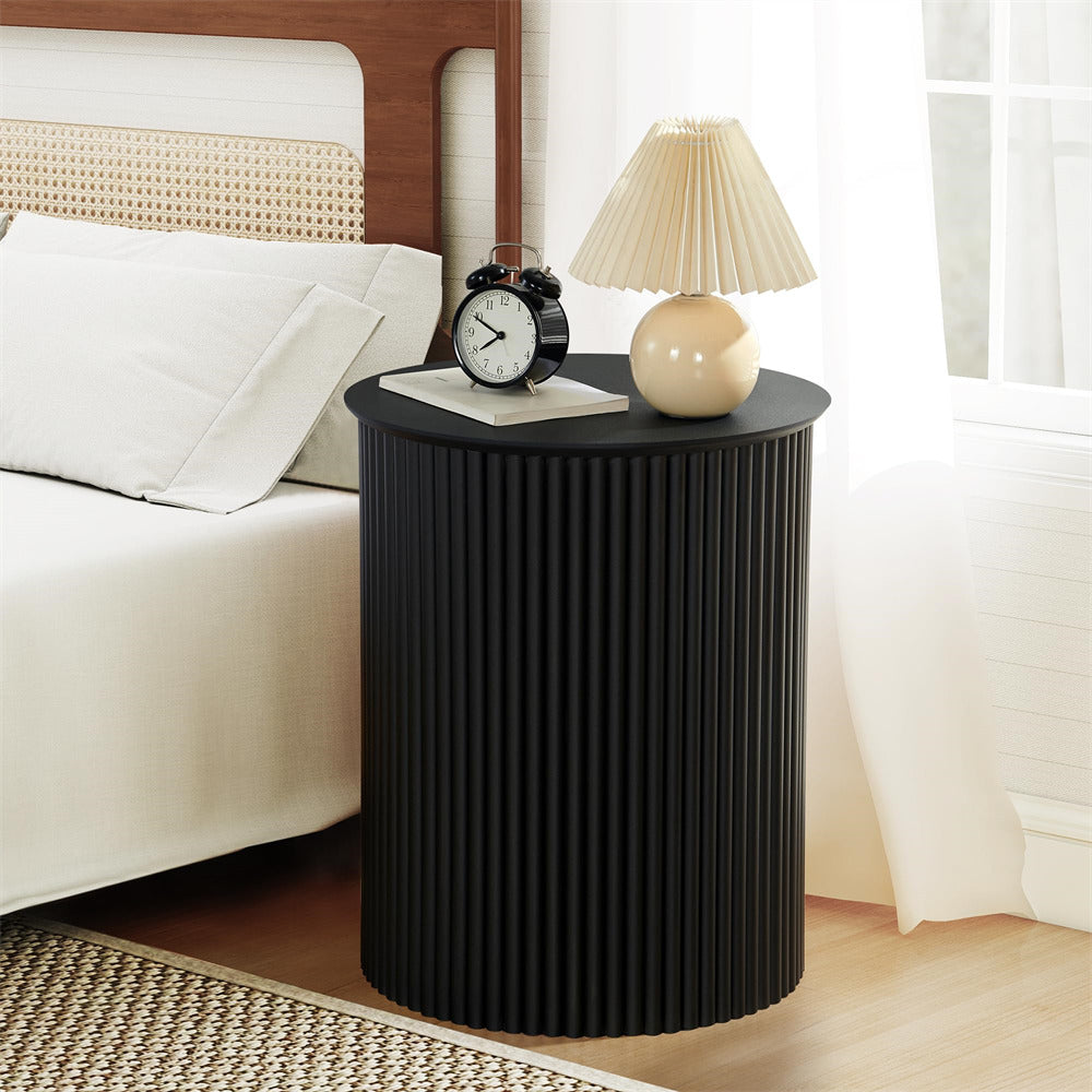 Black ribbed side table with a lamp and clock next to a white sofa in a bedroom.