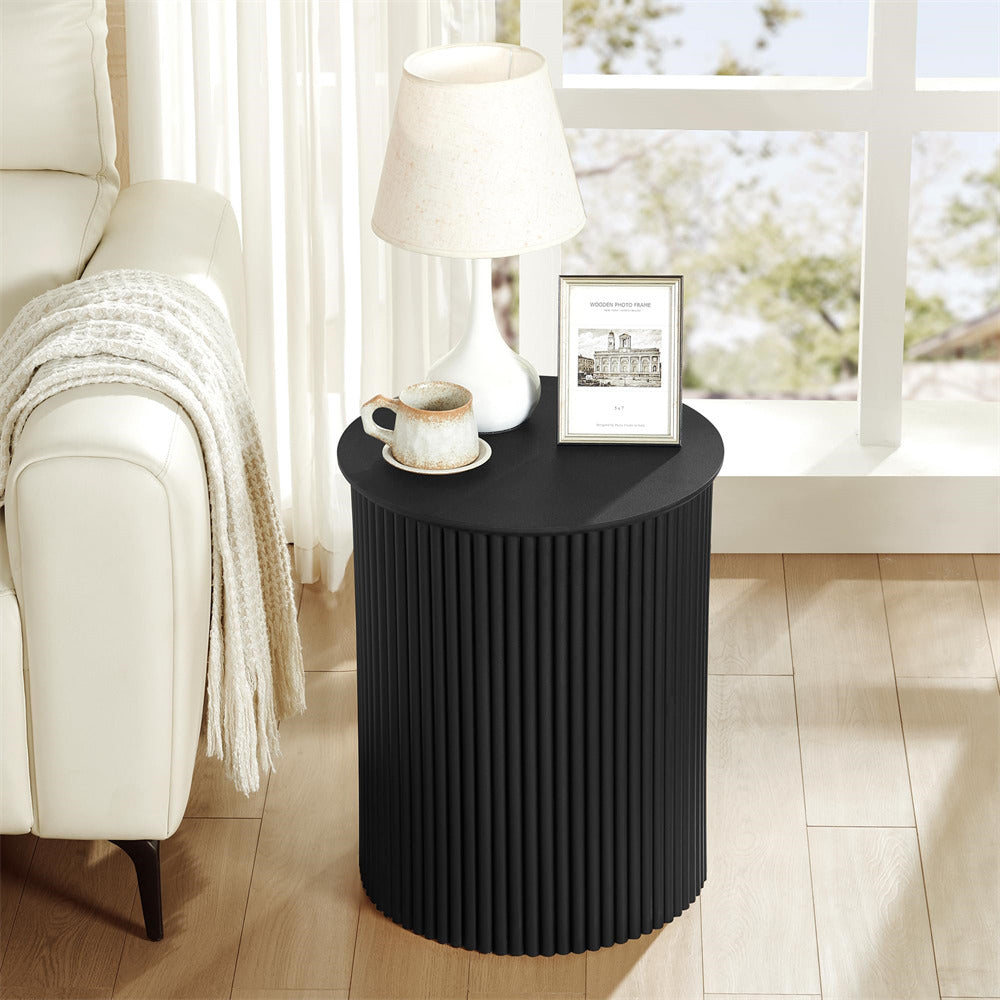 Black side table with a lamp, mug, and framed picture in a living room setting.