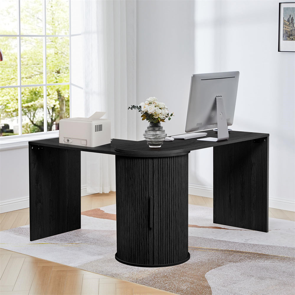 Black L-shaped desk with a computer setup in a bright room with large windows.