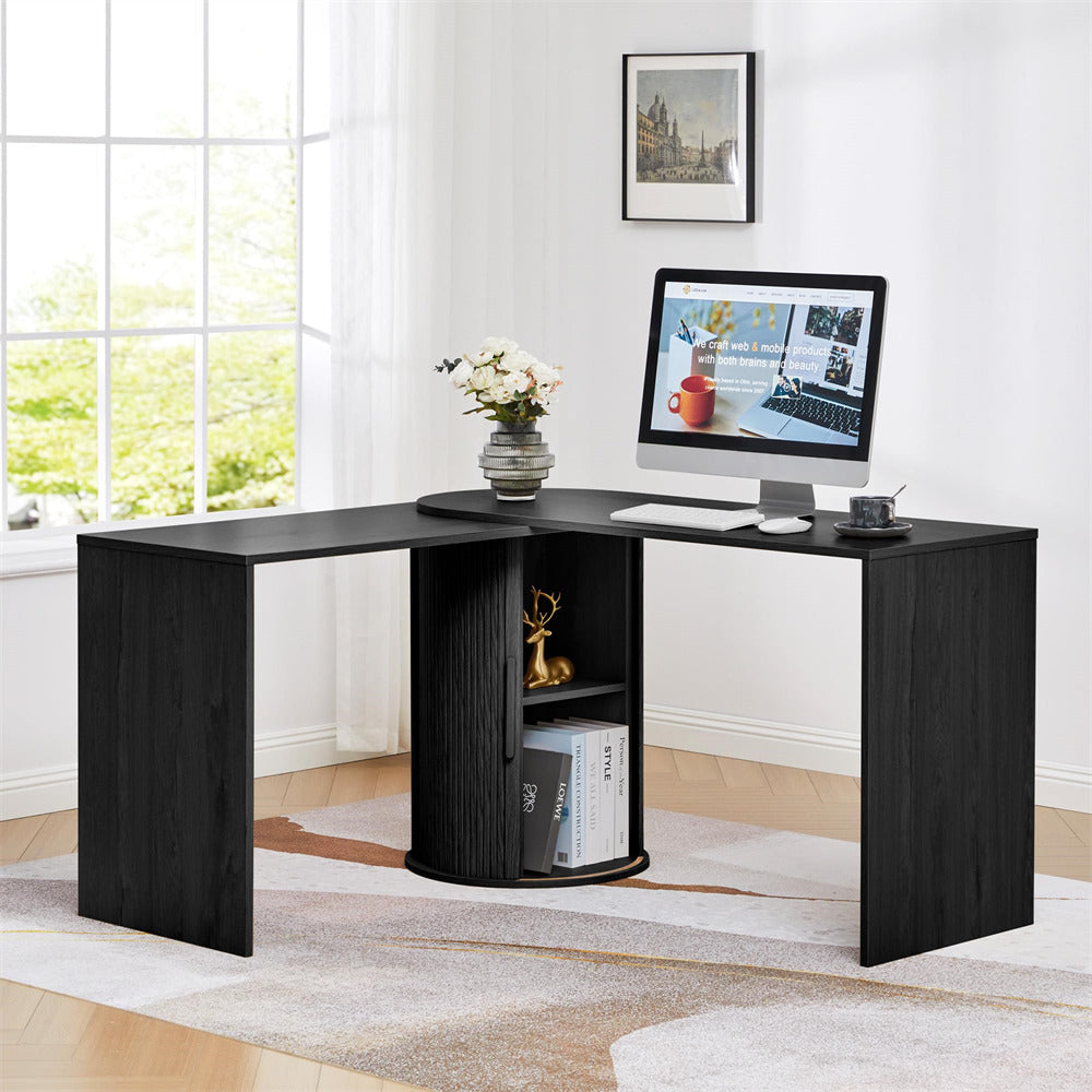 Black L-shaped desk with a computer setup in a bright room.
