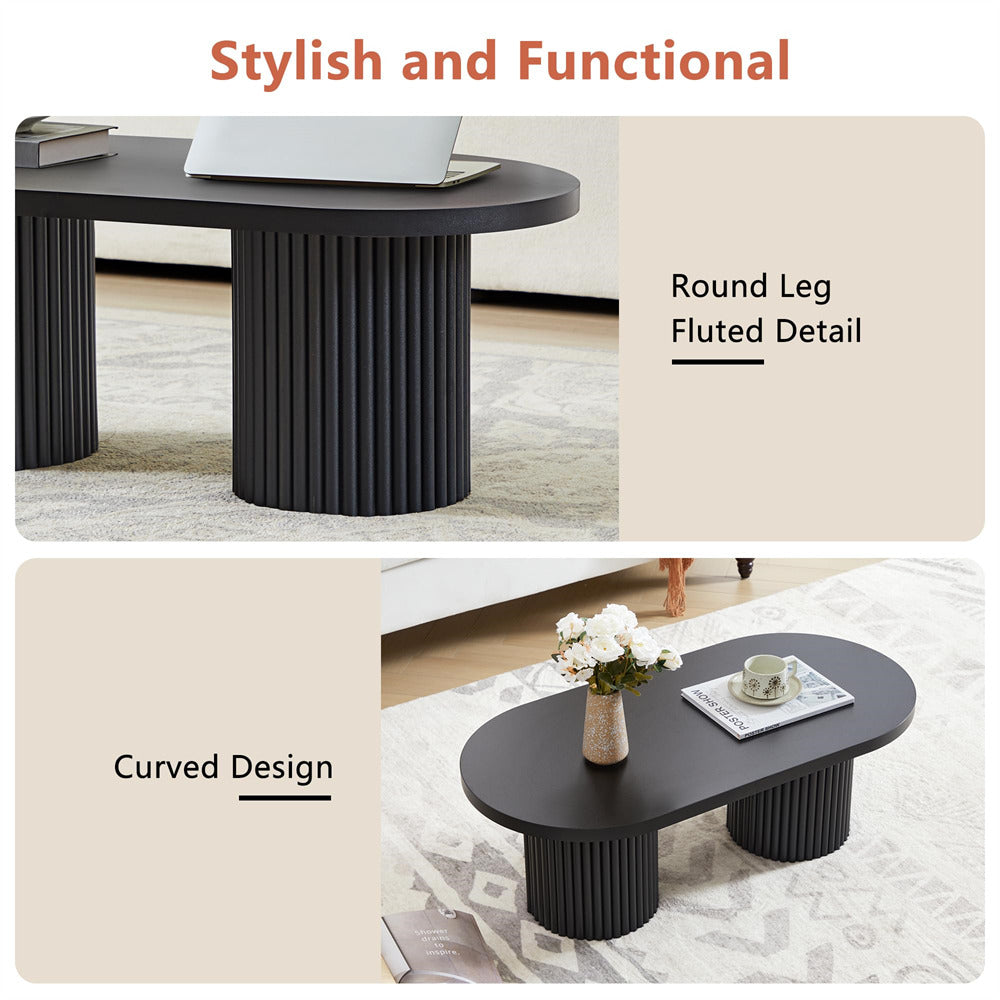 Black coffee table with round leg fluted detail and curved design in a room setting.