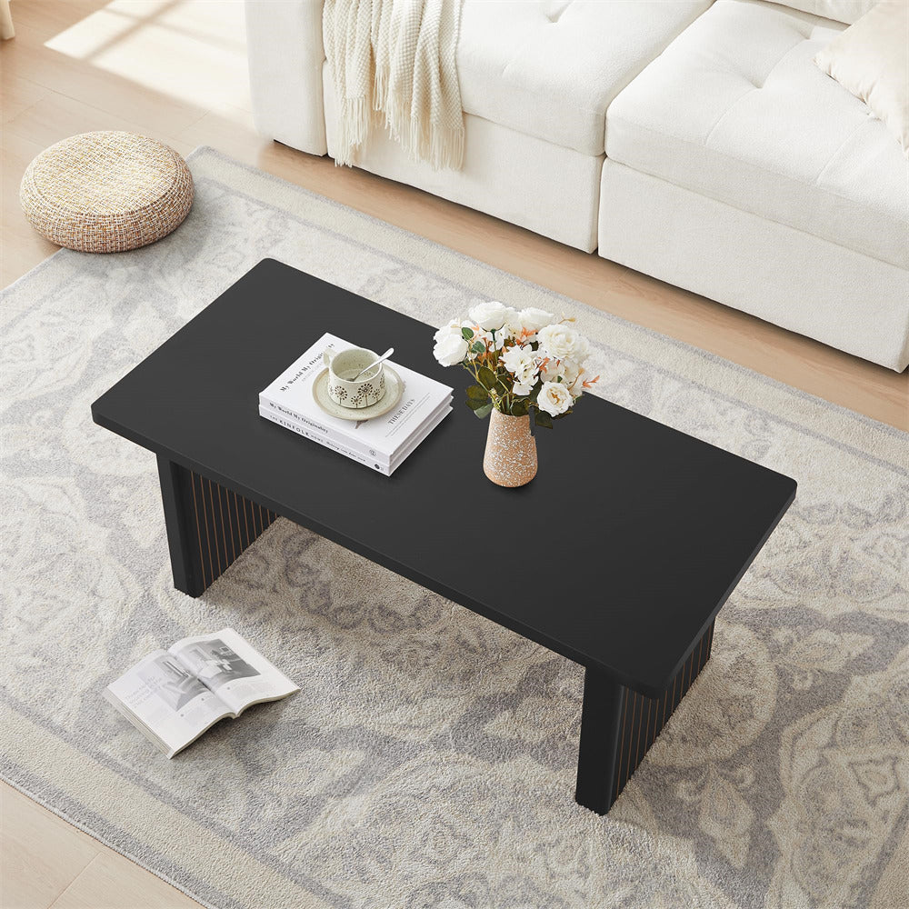 Black coffee table in a living room with a vase of flowers, books, and a cup.