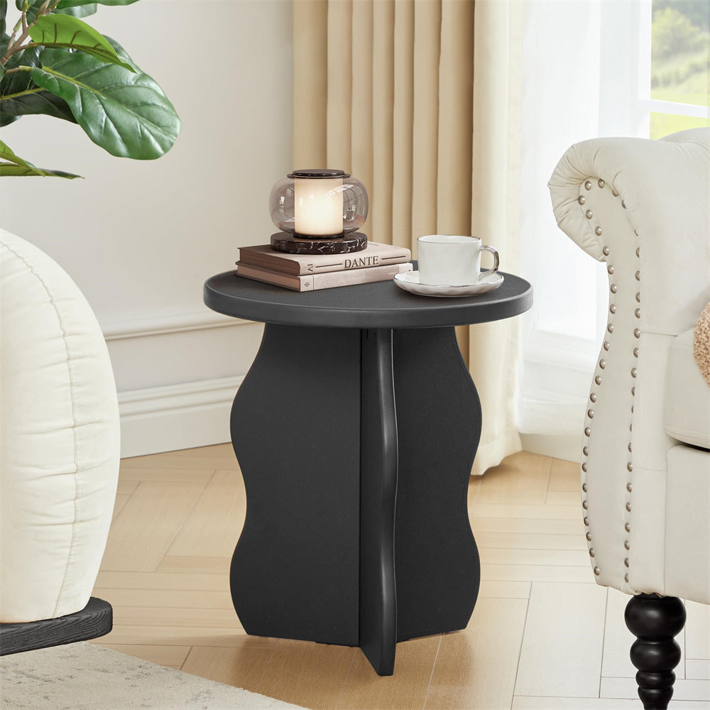 Black side table with a candle, books, and a mug in a living room setting.