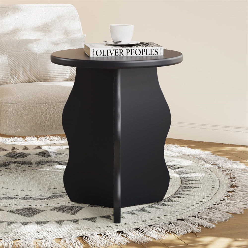 Black side table with a white cup and book titled 'Oliver Peoples' in a living room setting.