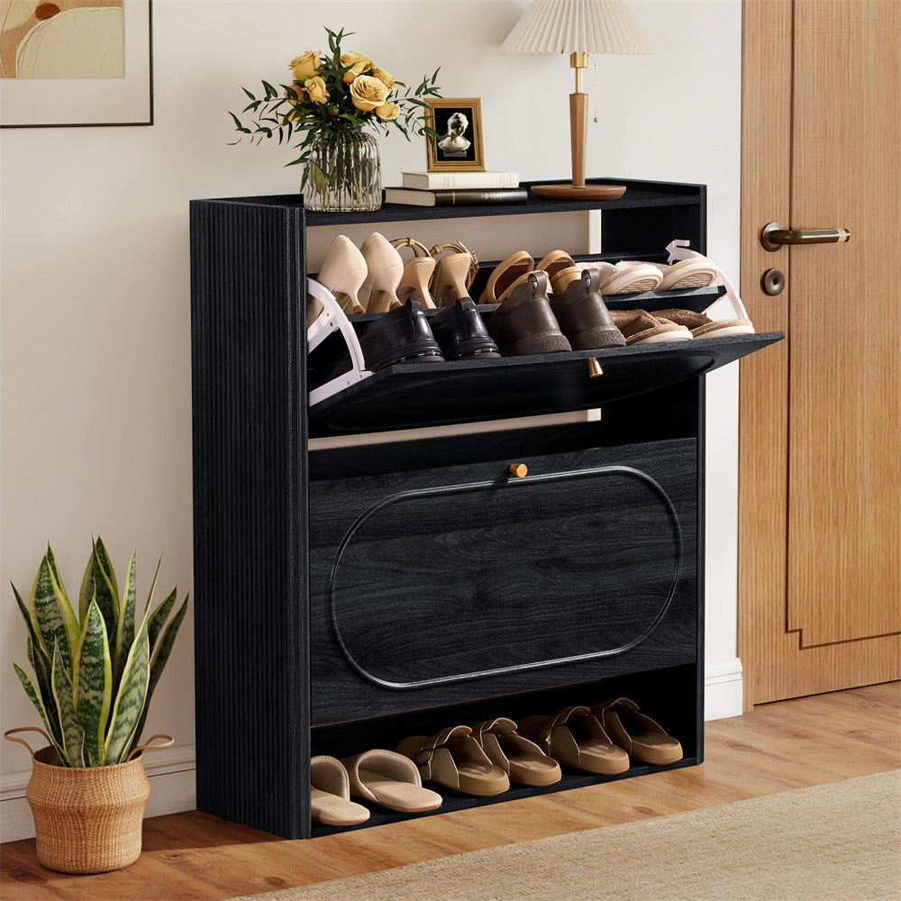 Black shoe cabinet with shoes on a wooden floor, next to a plant and a door.
