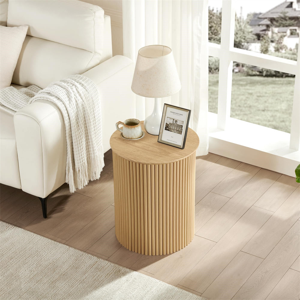 Round wooden side table with a lamp and mug in a living room setting.