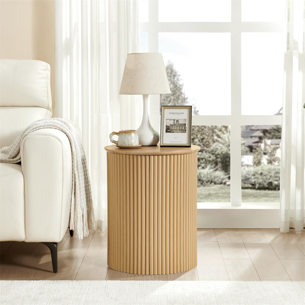 Beige side table with lamp and picture frame next to a white armchair in a bright room.