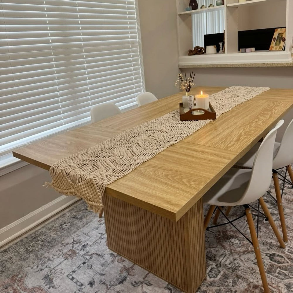 Wooden dining table with a macrame runner and candles in a home setting.