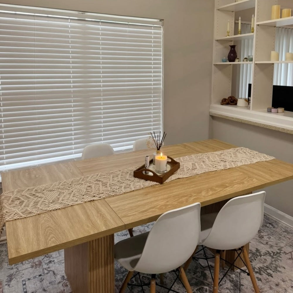 Dining room with wooden table, lace runner, and white chairs.
