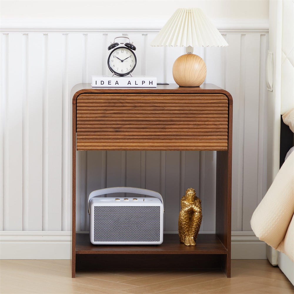 Wooden nightstand with decorative items including a lamp, clock, and books against a white wall.