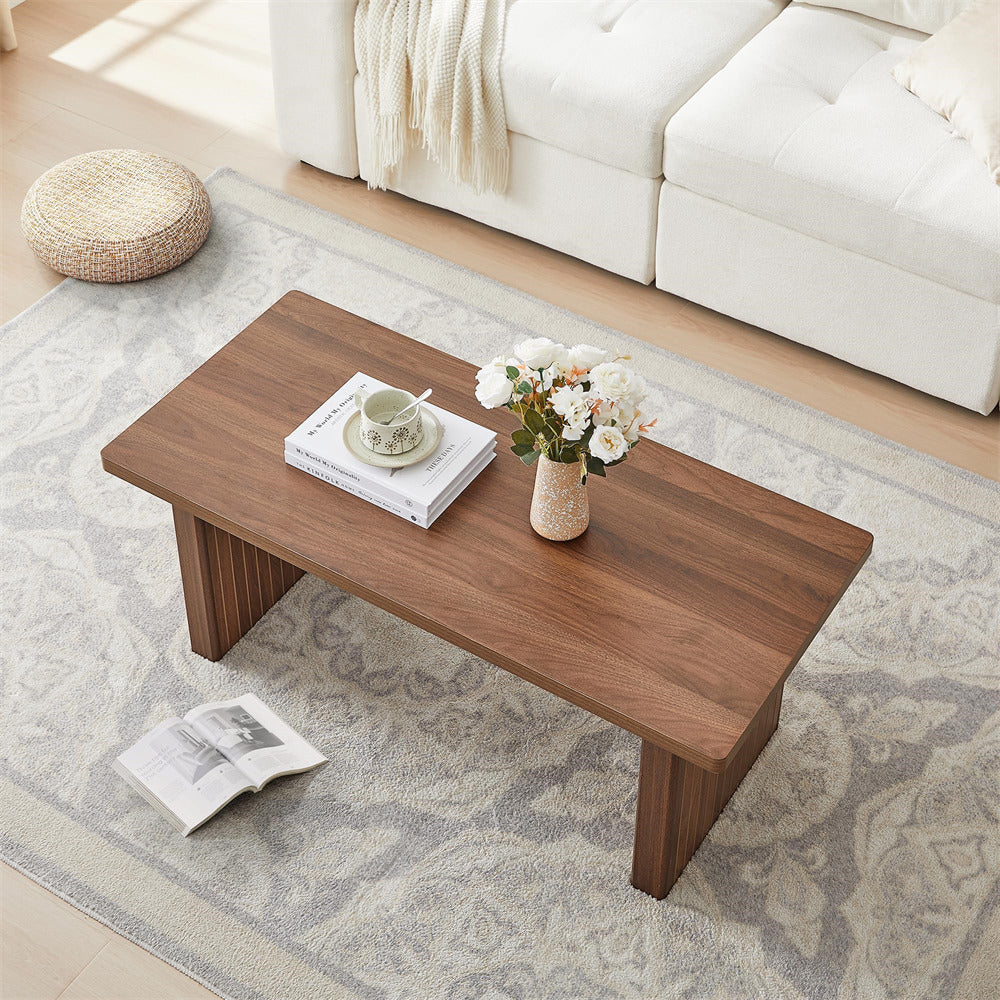 Wooden coffee table with books and a vase of flowers in a living room setting.