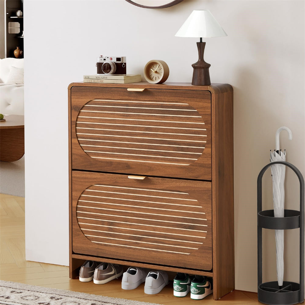 Wooden shoe cabinet with two drawers, shoes inside, and decor items on top in a room setting.