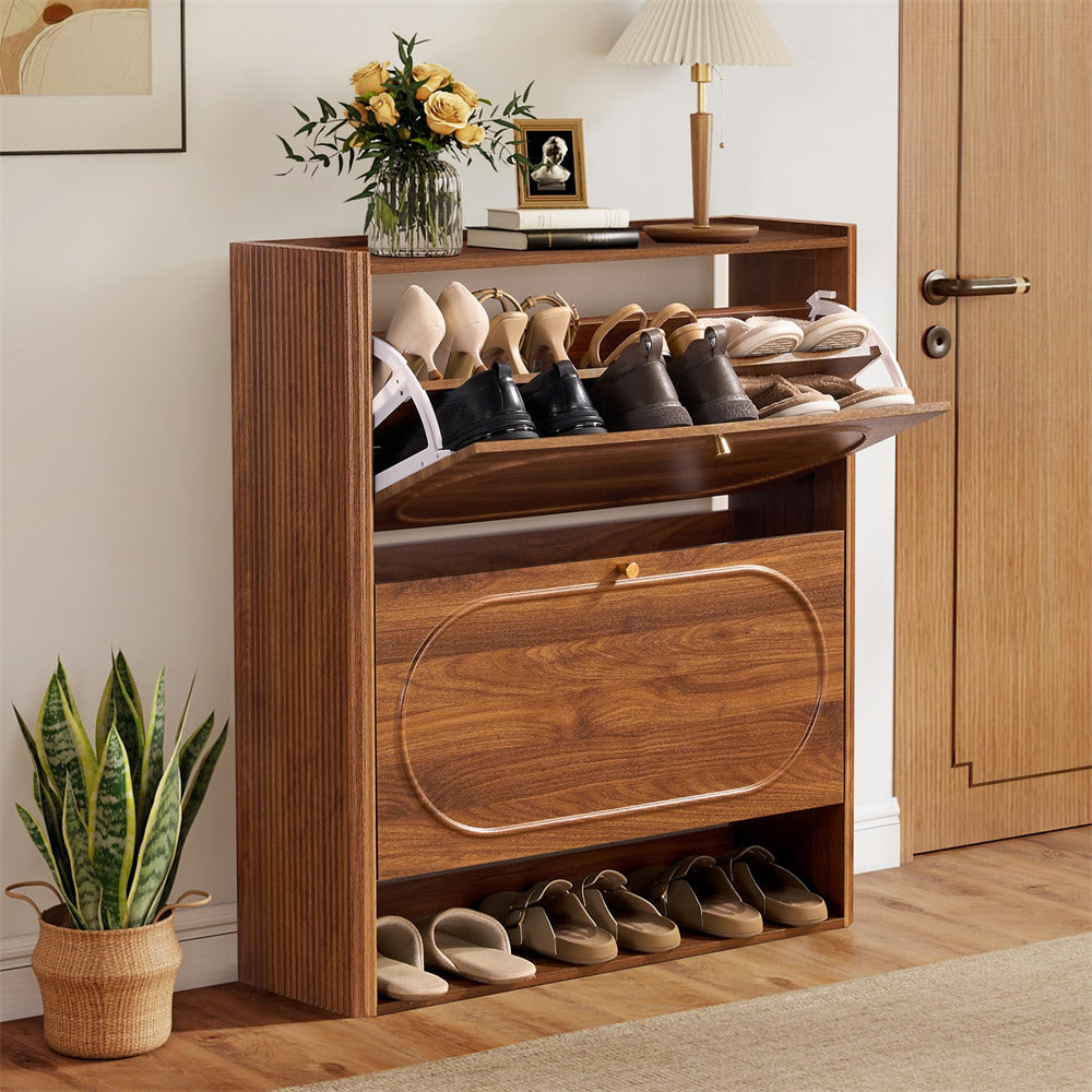 Wooden shoe cabinet with open door displaying shoes, next to a plant and a vase with flowers.
