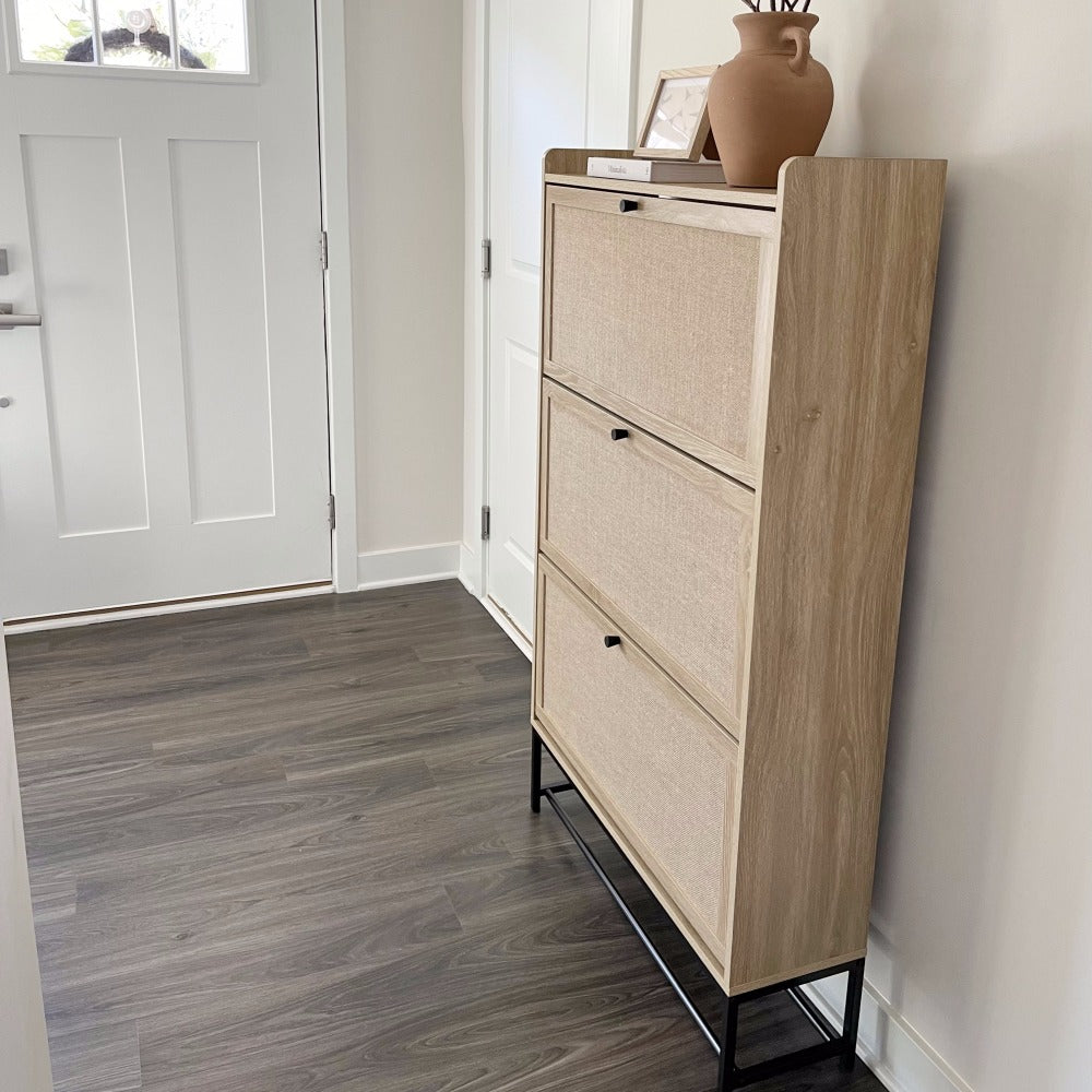 Wooden shoe cabinet with three drawers in a room with a white door and gray floor.