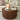 A round wooden coffee table with a fluted slatted front, styled in a living room setting with a beige sofa, patterned pillows, a ceramic vase with greenery, books, and candles on top.