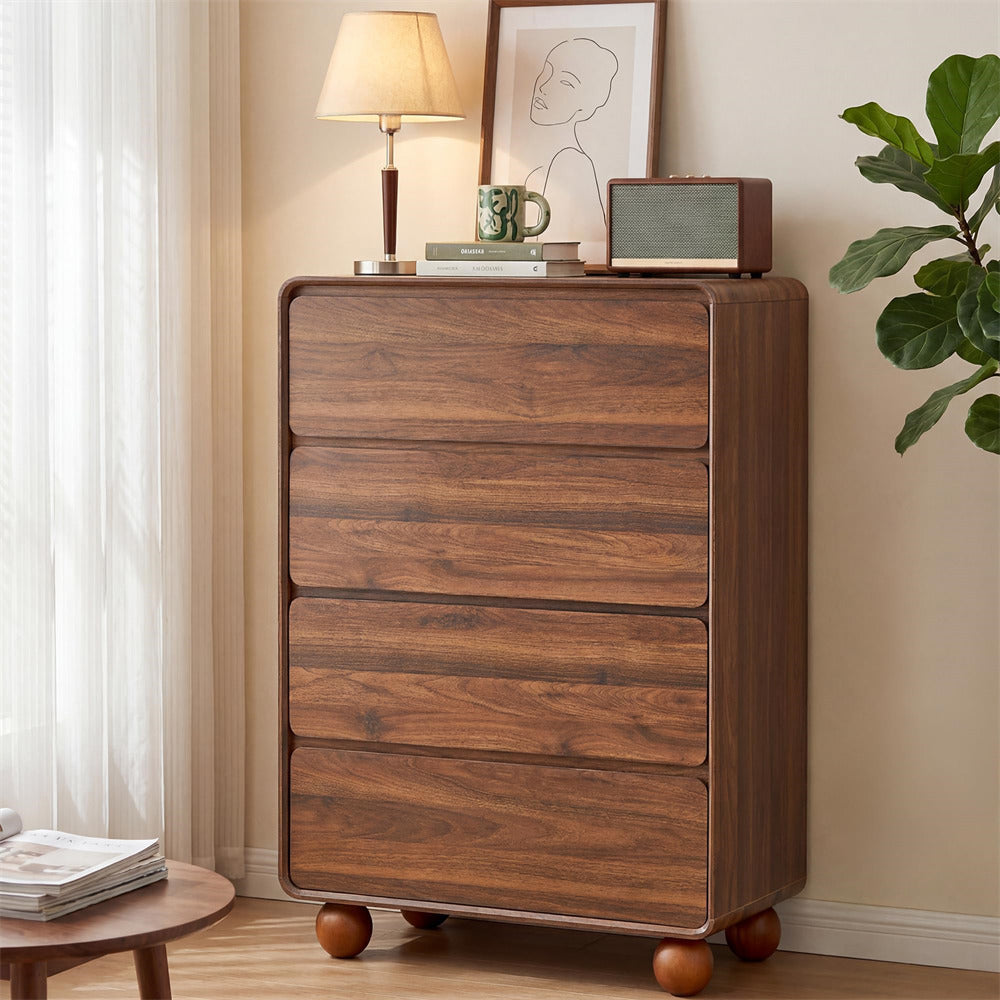 A tall wooden five-drawer chest of drawers with rounded feet, styled in a warm, neutral-toned room next to a window with sheer curtains, a potted plant, and various decorative items on top.