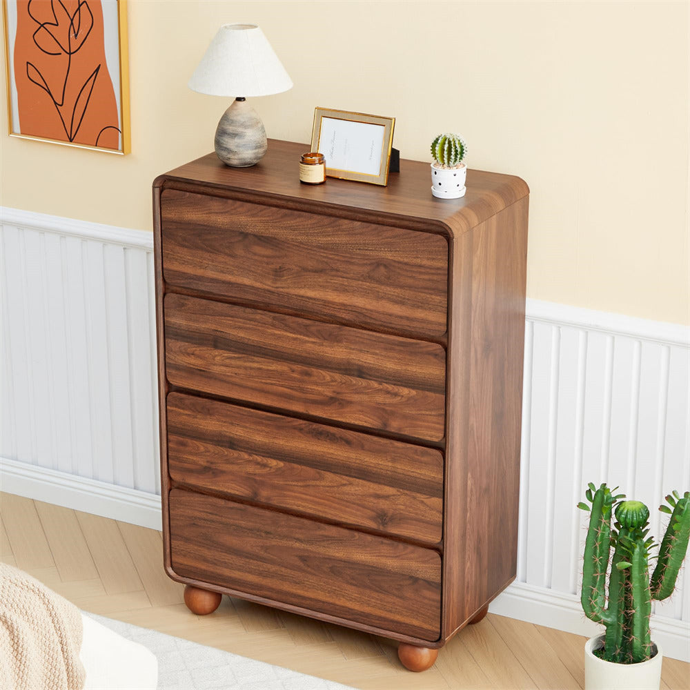 A five-drawer wooden dresser with a warm medium-brown finish and rounded feet, styled in a bedroom corner with a lamp, picture frame, small cactus, and a larger potted cactus against a beige wall with white wainscoting.