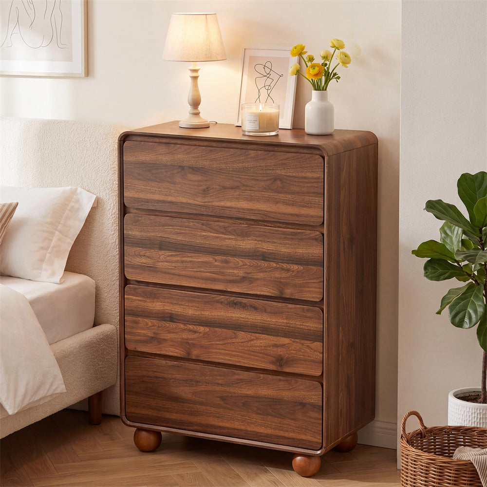 A dark brown wooden five-drawer chest of drawers styled in a cozy bedroom corner next to a bed, topped with a table lamp, candle, and small vase of yellow flowers.