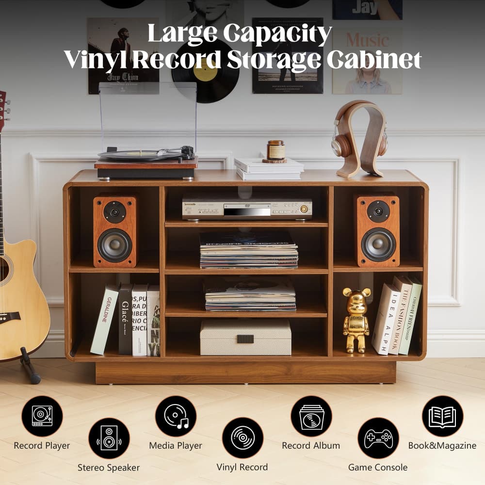 A large wooden vinyl record storage cabinet with open shelves and side speakers, shown in a styled room setting with record players, headphones, books, and a gold figurine. White text at the top reads 'Large Capacity Vinyl Record Storage Cabinet,' and feature icons along the bottom list included storage compartments, record player, media player, stereo speaker, vinyl record, game console, and book&magazine storage.