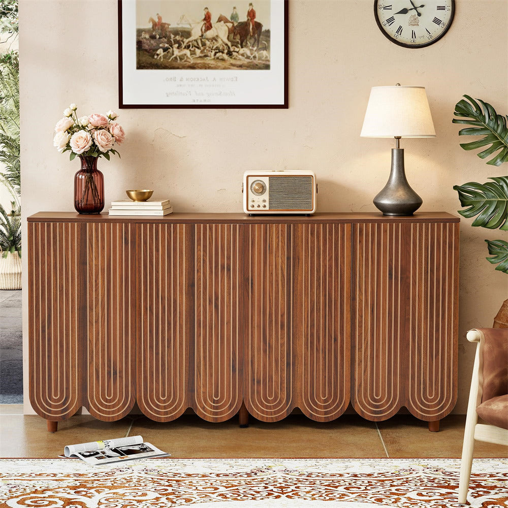 A mid-century modern wooden sideboard cabinet with vertically fluted panel doors, styled in a warm living room setting with a lamp, radio, flowers, and framed art.