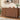 A wooden sideboard or credenza with a rich walnut finish, featuring a fluted vertical rib design and scalloped lower panels. The cabinet is styled in a modern kitchen setting with a wooden shelf, hanging mugs, a glass bottle, and decorative items on top.