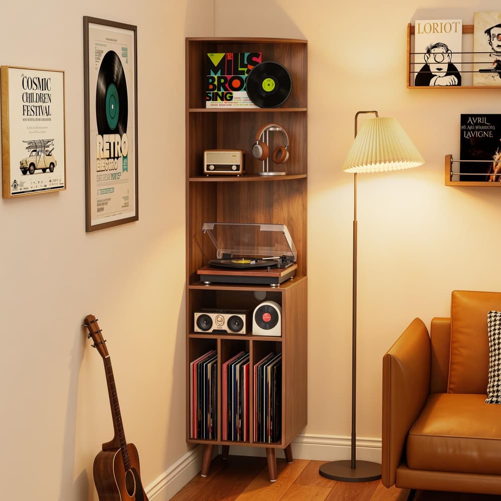 A tall wooden shelving unit in a cozy room corner, styled with vinyl records, speakers, headphones, a turntable, framed posters, a guitar, a floor lamp, and part of an orange-brown leather sofa.