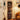 A tall wooden shelving unit in a cozy room corner, styled with vinyl records, speakers, headphones, a turntable, framed posters, a guitar, a floor lamp, and part of an orange-brown leather sofa.