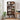 A tall wooden bookcase with five open shelves stands in a bright room beside a window, holding books, baskets, framed photos, plants, and small decor items. A small wooden desk with a plant and clock is visible on the right.