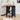 Black woven side table with books, fruit basket, and vase in a living room setting.