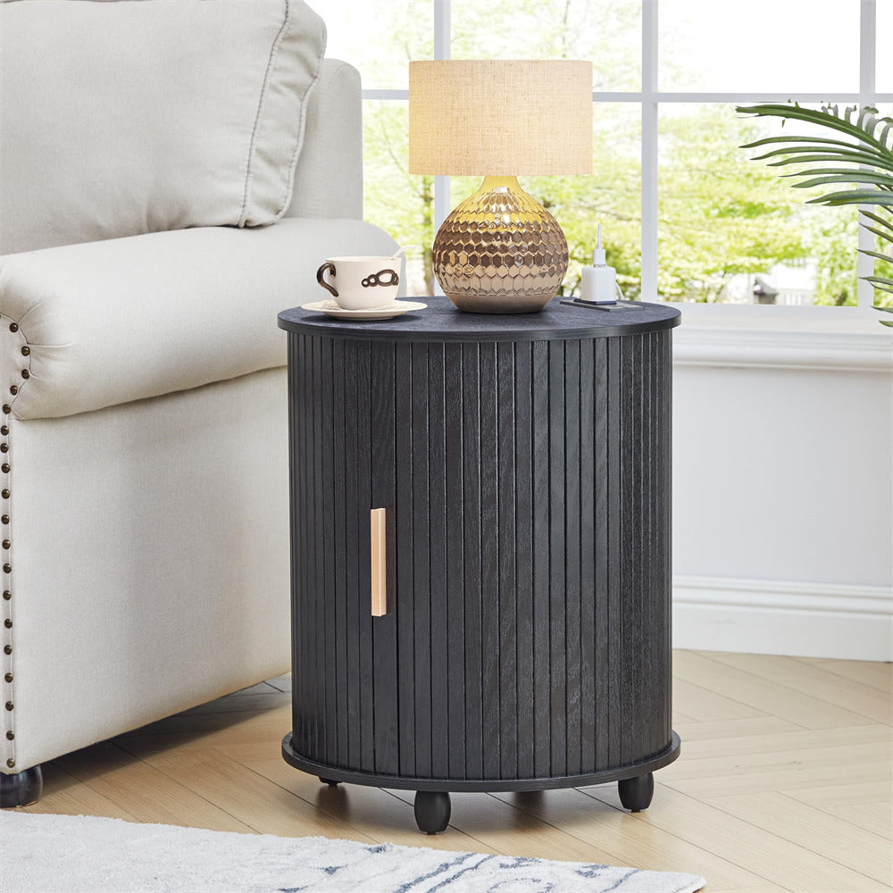 Black cylindrical side table with a lamp and cup in a living room setting.