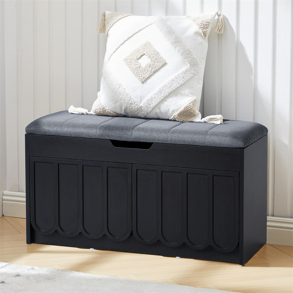 Black shoe storage bench with gray cushion and decorative pillow on a light wooden floor.