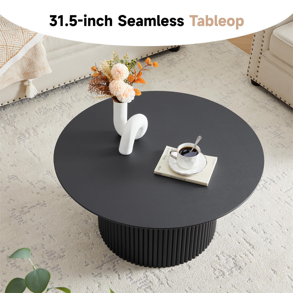 Black round coffee table with a vase of flowers and a cup on a light-colored floor.