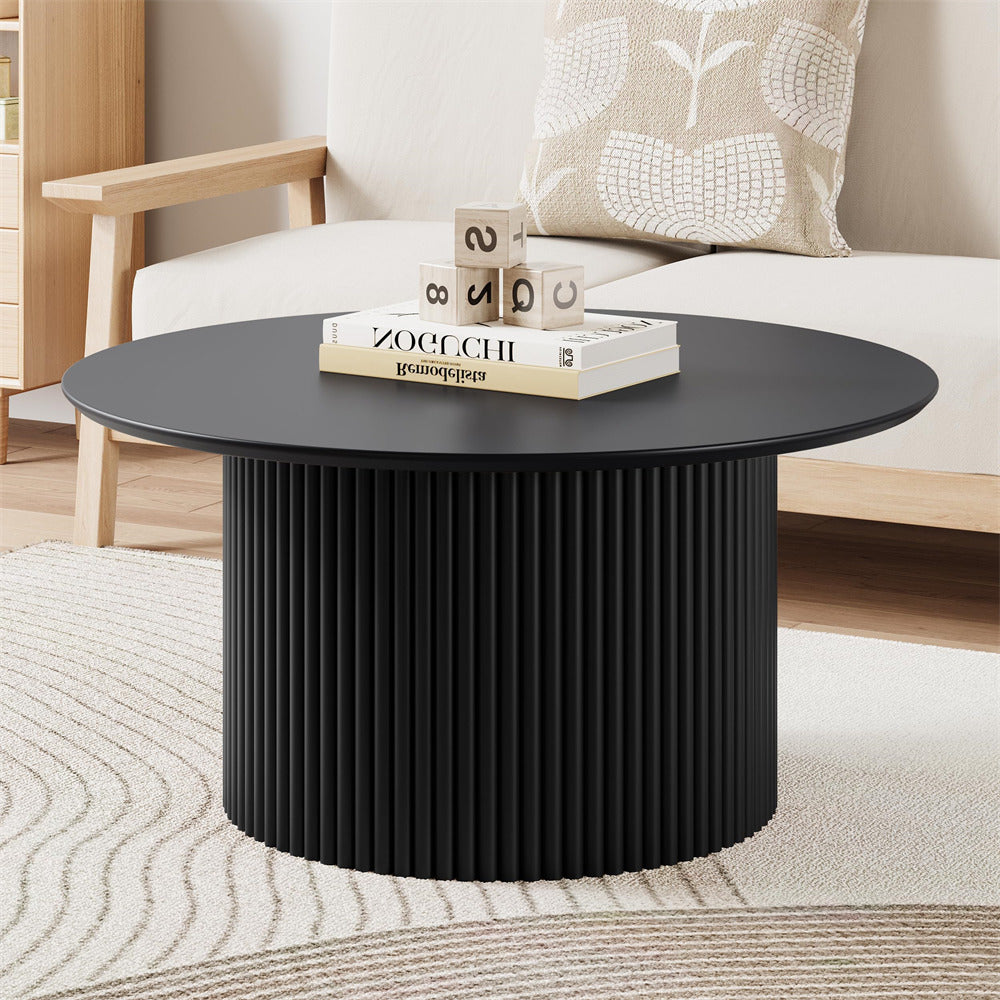 Black round coffee table in a living room setting with books and decorative items.