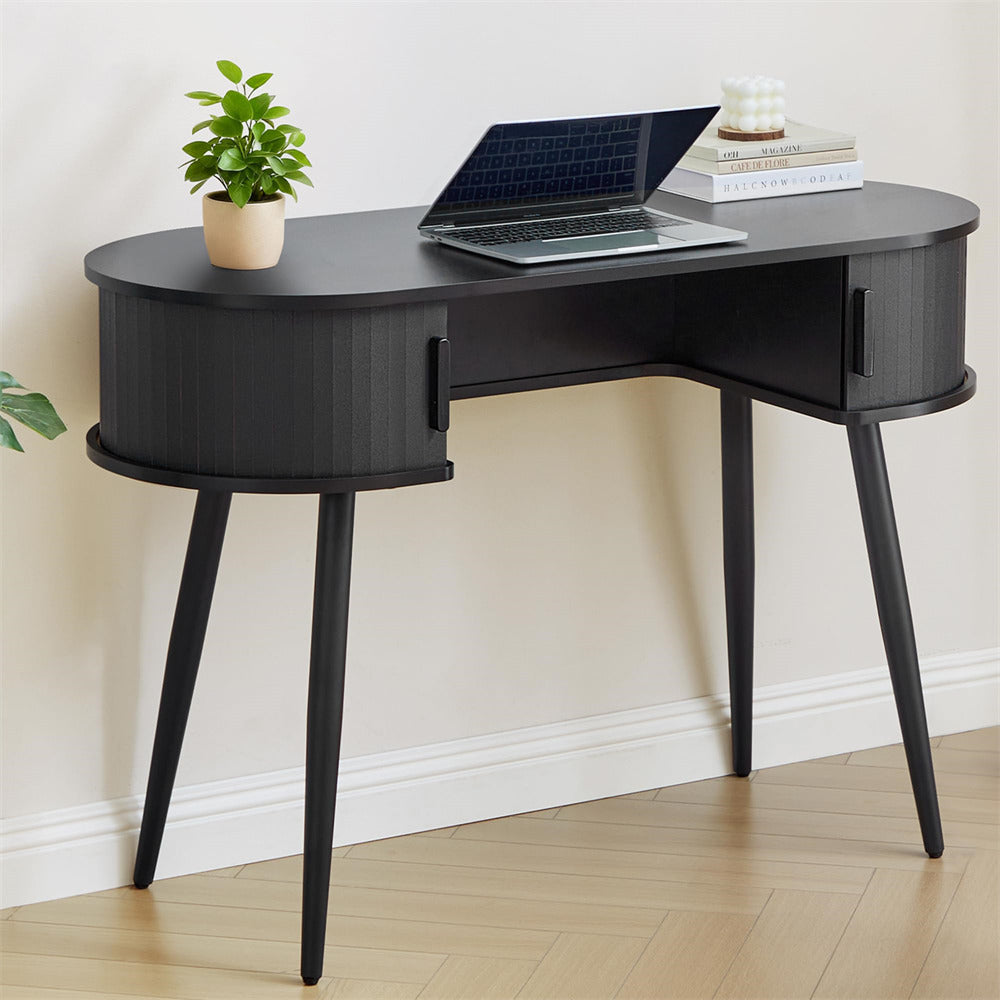 Black desk with a laptop, plant, and books on a light wood floor.