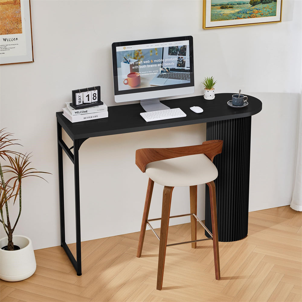 Modern home office setup with a black desk, computer monitor, and wooden stool.