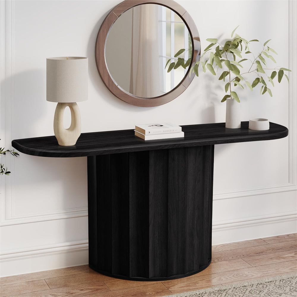 Black console table with round mirror, lamp, and books against a white wall.