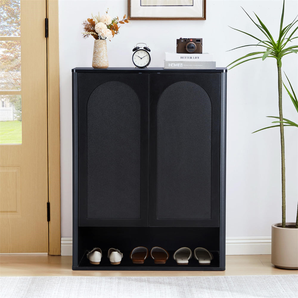Black shoe cabinet with shoes underneath, placed in a room with a plant and a door.