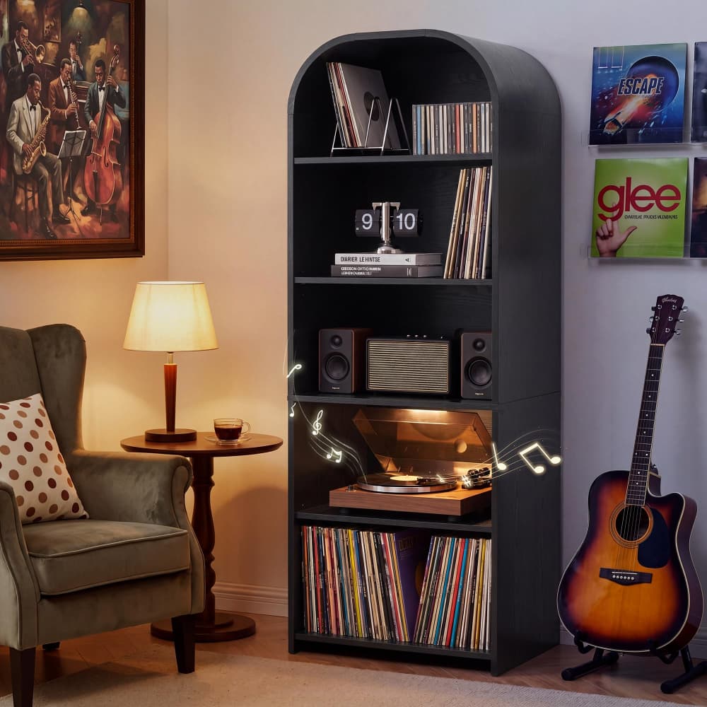 A tall black arched bookshelf filled with vinyl records, speakers, a turntable, and books, placed in a cozy living room next to an armchair and guitar.