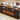 Black electric fireplace TV stand console with a wood-look top, glowing faux logs, three open storage drawers, and a USB charging socket on the side. Text at the top reads '3 STORAGE DRAWERS USB CHARGING SOCKET' with a circular inset showing the charging port detail.