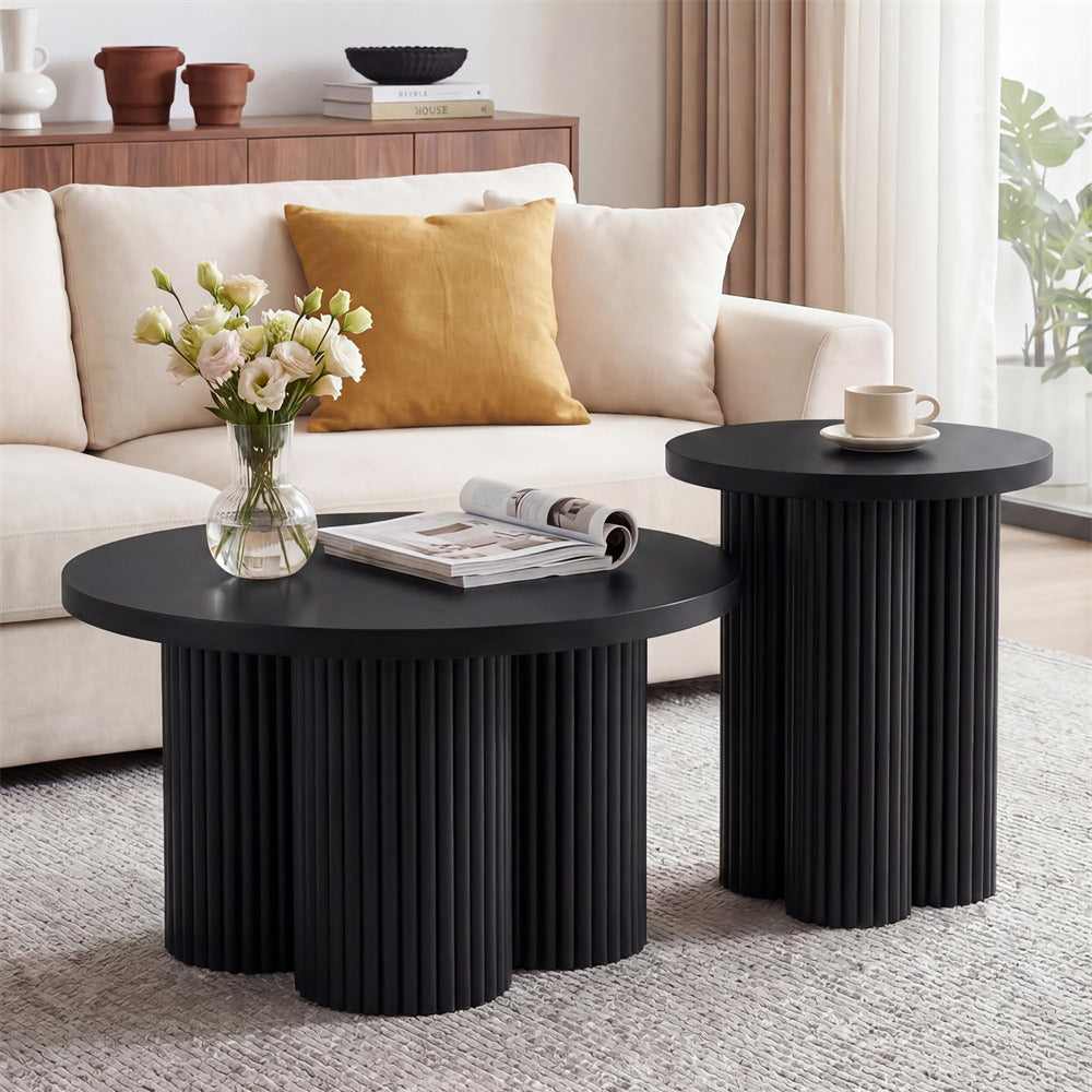 A modern black coffee table with a fluted pedestal base and a matching round side table, styled in a bright living room next to a cream sofa.