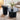 Two modern nesting coffee tables in a dark charcoal gray fluted base, styled in a bright living room with a white ceramic vase of greenery on the larger round table and books on the smaller side table.