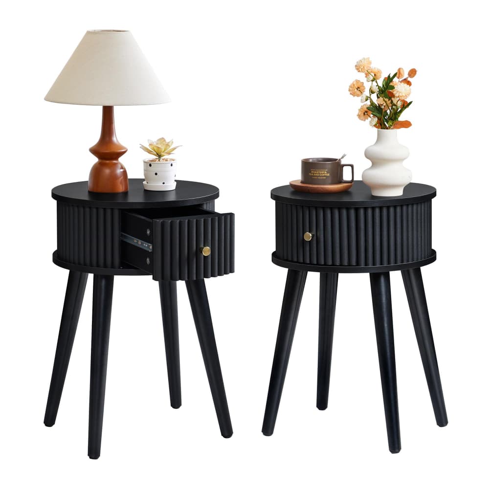 Two black round side tables with ribbed fronts and tapered legs, shown on a white background. The left table has a lamp and small vase, and the right table has a mug and flower vase.