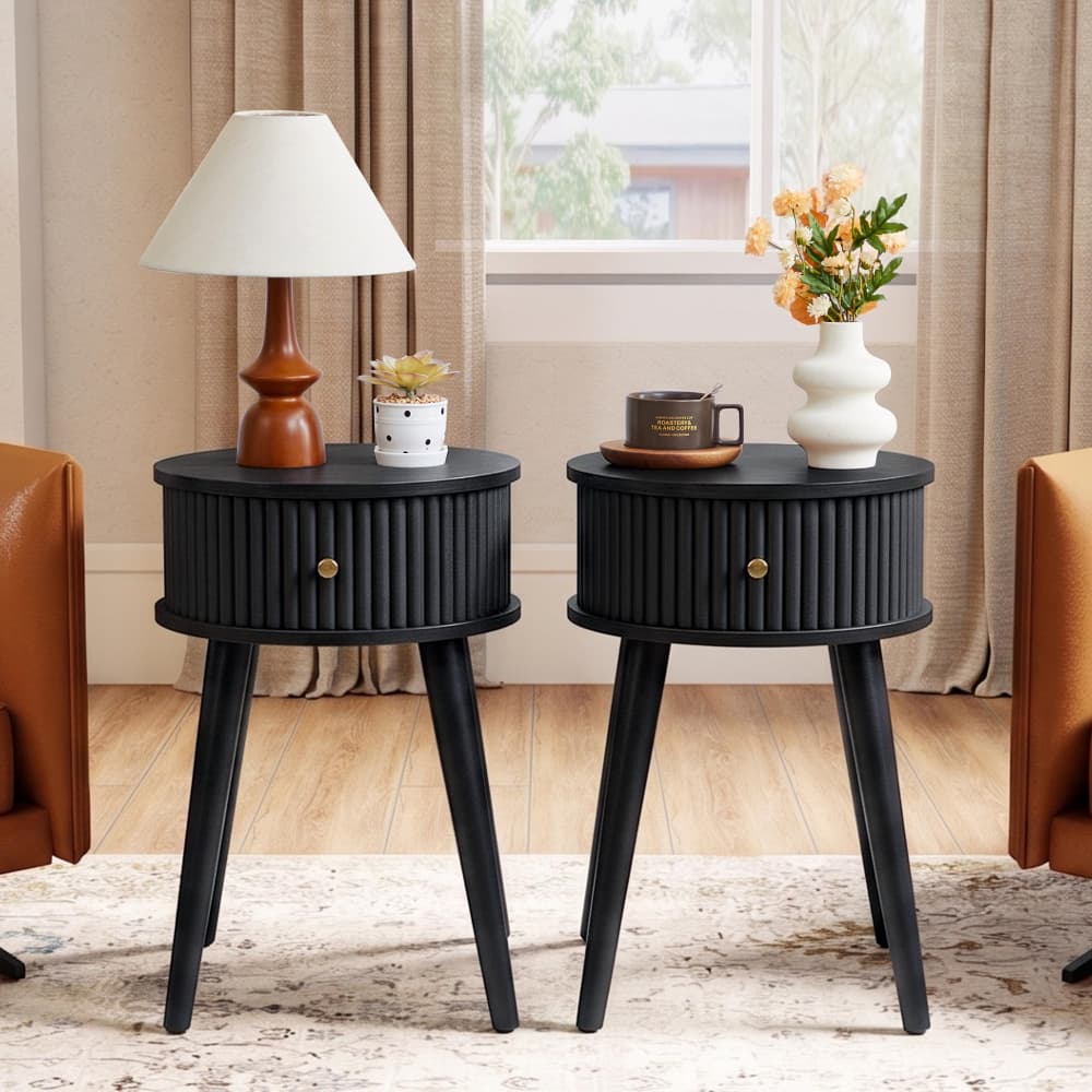 Two matching black ribbed nightstands with tapered legs, styled in a living room setting with a lamp, mug, and vase of flowers on top.