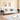 A cream-colored upholstered sofa with a light wood base and legs, styled in a warm, modern living room with two side tables, a lamp, and two framed abstract art prints on the wall.