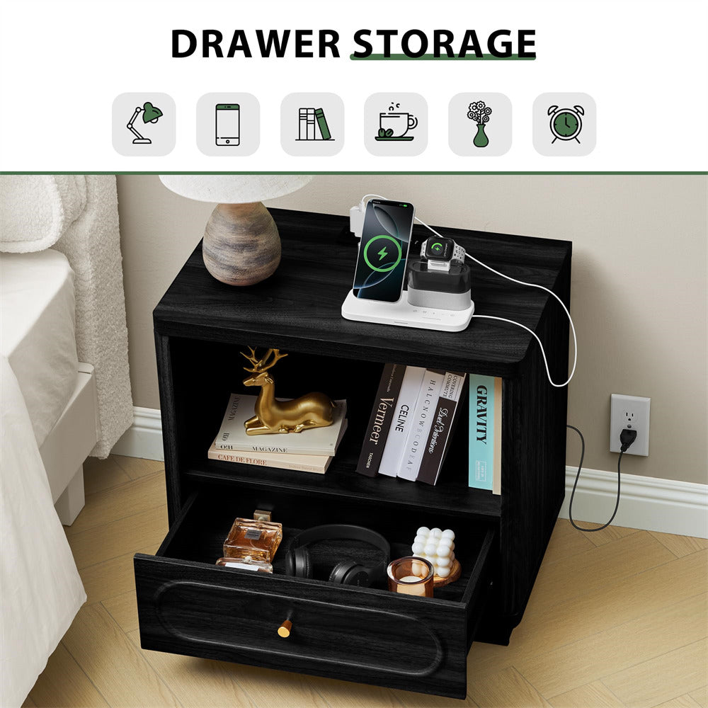 Black drawer storage unit with a lamp, books, and electronic devices on a bed side table.