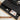 Black desk with open drawer containing office supplies on a light wooden floor.
