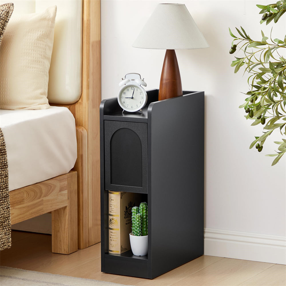 Black nightstand with lamp, clock, and books next to a bed with pillows and a plant.