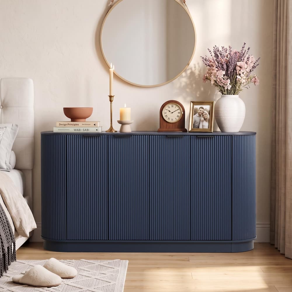 A navy blue ribbed sideboard or credenza in a styled bedroom setting, topped with a candlestick, books, a bowl, a clock, a framed photo, and a white vase with dried flowers.