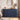 A navy blue ribbed sideboard or credenza in a styled bedroom setting, topped with a candlestick, books, a bowl, a clock, a framed photo, and a white vase with dried flowers.