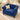 A royal blue velvet Chesterfield armchair with button tufting and silver nailhead trim, styled with a beige throw pillow in a bright, sunlit room on a textured rug.